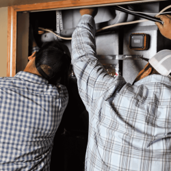 The image shows the back of two HVAC experts installing a furnace.