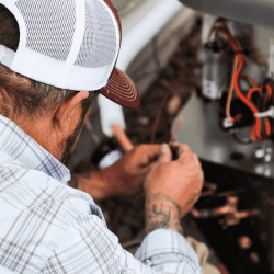 The image shows a close-up of an HVAC technician working on the wiring system of an HVAC unit.